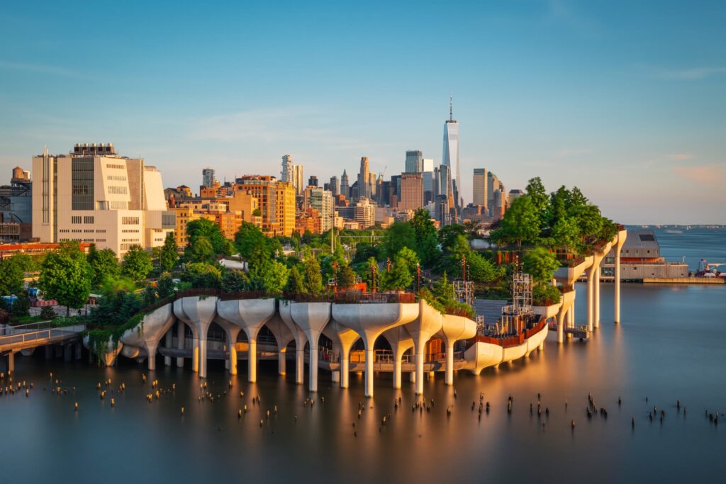 Little Island's tulip-shaped concrete piles and tree-covered top on the Hudson River at golden hour, with Lower Manhattan behind