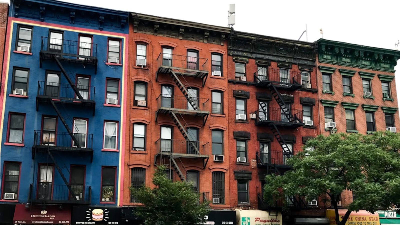 Colorful apartment buildings with fire escapes and trees lining a New York City street