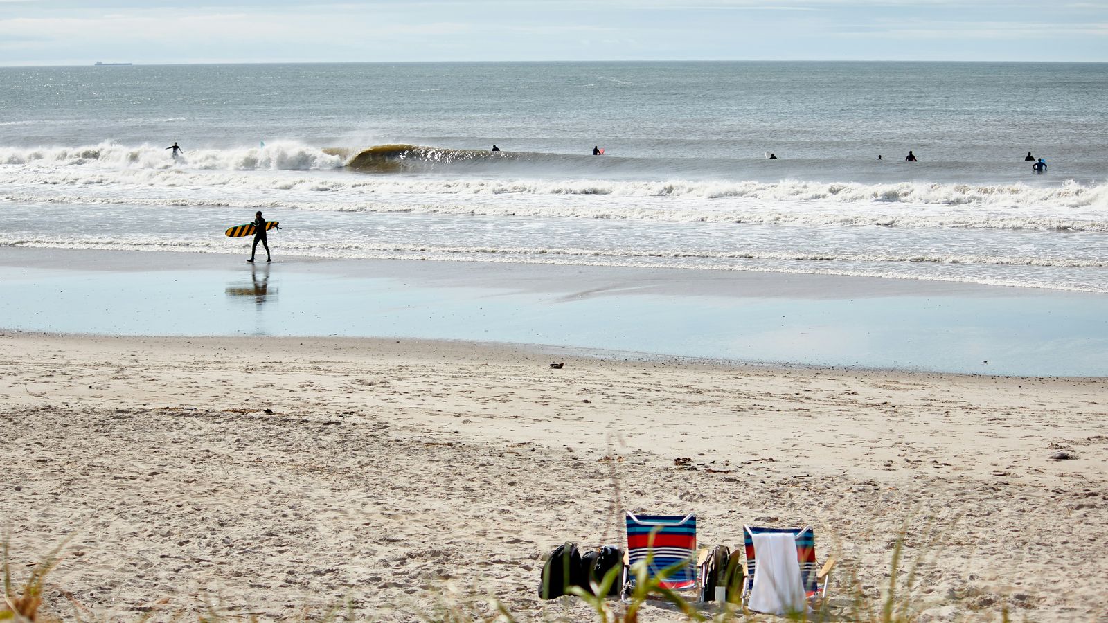 Surfer walking on Rockaway Beach Queens New York with waves breaking and beach chairs in the foreground