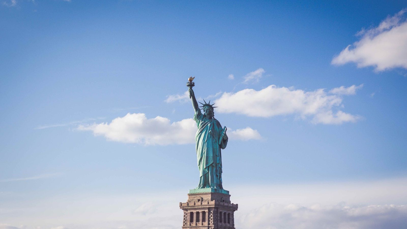 The Statue of Liberty standing against a blue sky, the iconic welcome for millions of immigrants arriving in New York