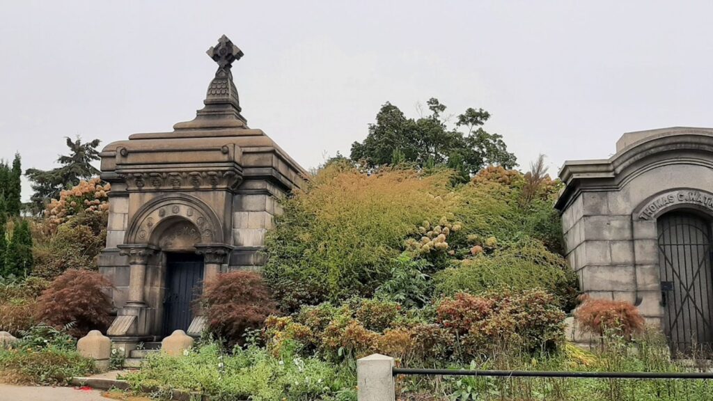Victorian stone mausoleums surrounded by autumn foliage in a historic cemetery — the kind of landscape that inspired New York's great parks