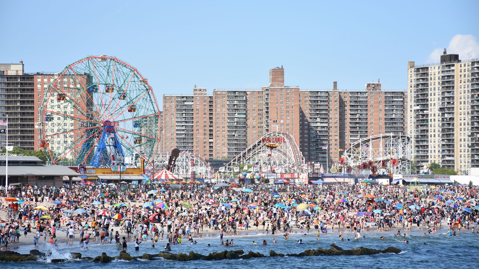 Coney Island beach in Brooklyn with Luna Park amusement rides and the New York coastline on a summer day