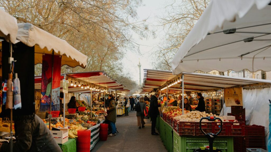 Outdoor farmers market stalls filled with fresh fruit and vegetables under white canopies on an autumn day