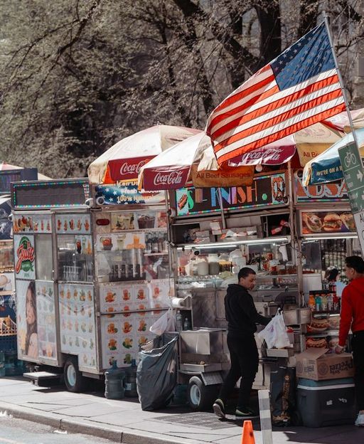 Food vendor carts lined up on a Manhattan sidewalk with an American flag flying above them on a spring day in New York City
