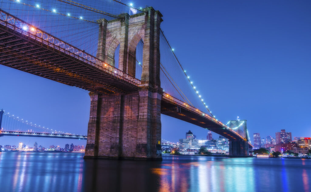 The Brooklyn Bridge lit up at night and reflected in the East River