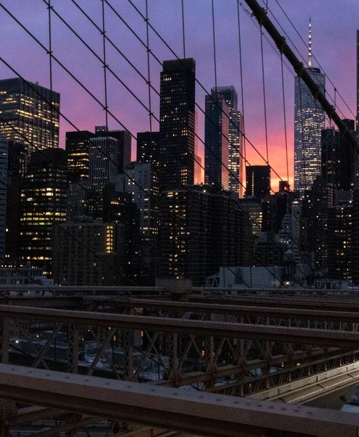 New York City skyline glowing at dusk, viewed from the Brooklyn Bridge