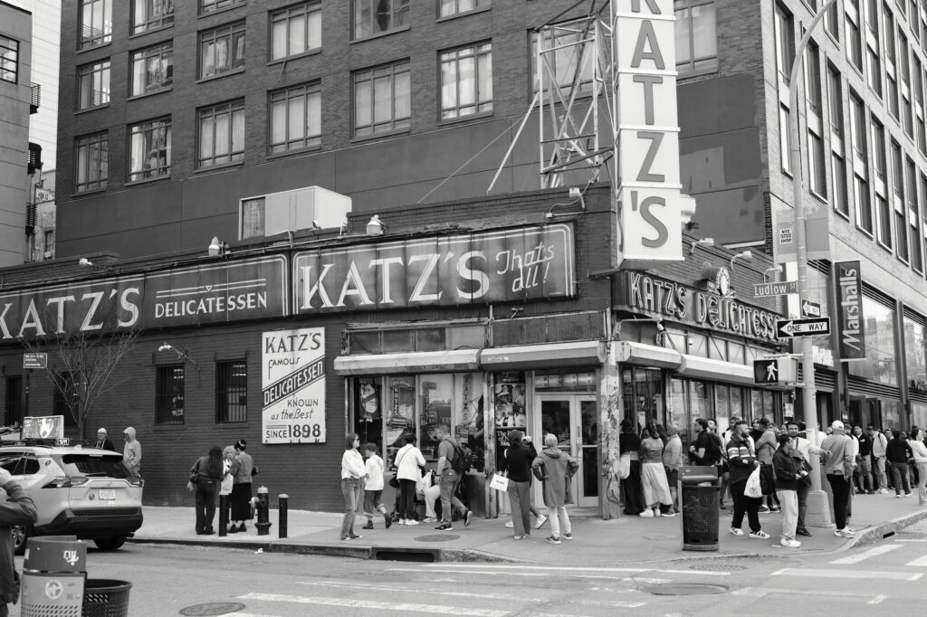 Black-and-white photo of Katz's Delicatessen at Houston and Ludlow Streets, with a line of people outside