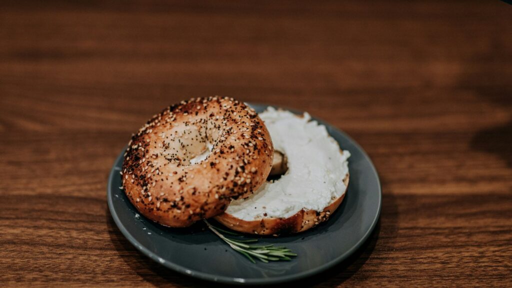 A classic New York everything bagel with cream cheese, served on a dark plate — a city staple for over a century