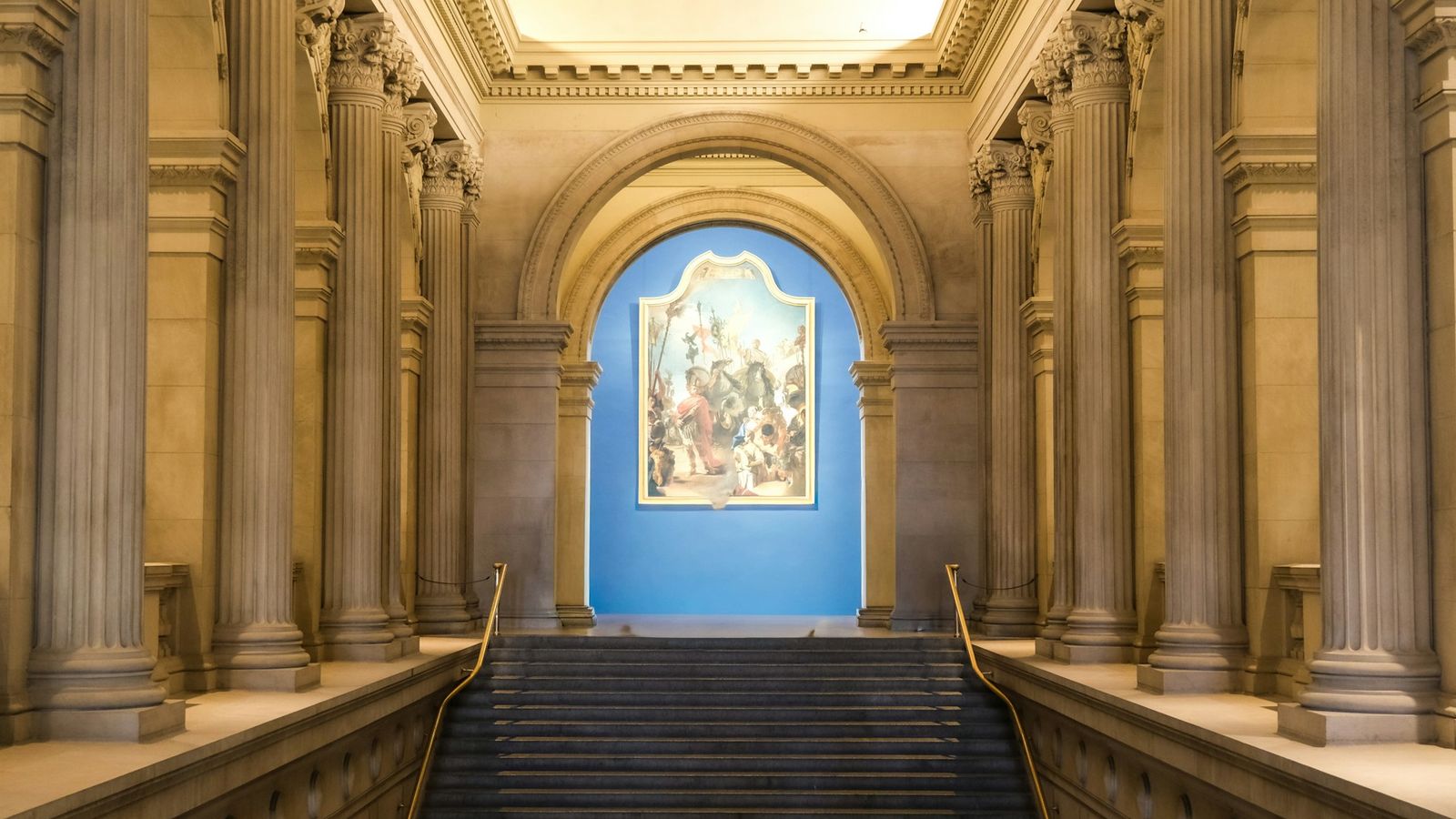 Grand classical interior with tall Corinthian columns, marble staircase, and large oil painting at the Metropolitan Museum of Art, New York City