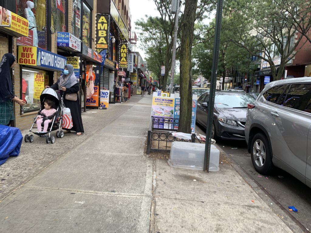 Shoppers passing jewelry and clothing stores with Bengali signs on 74th Street, Jackson Heights, Queens