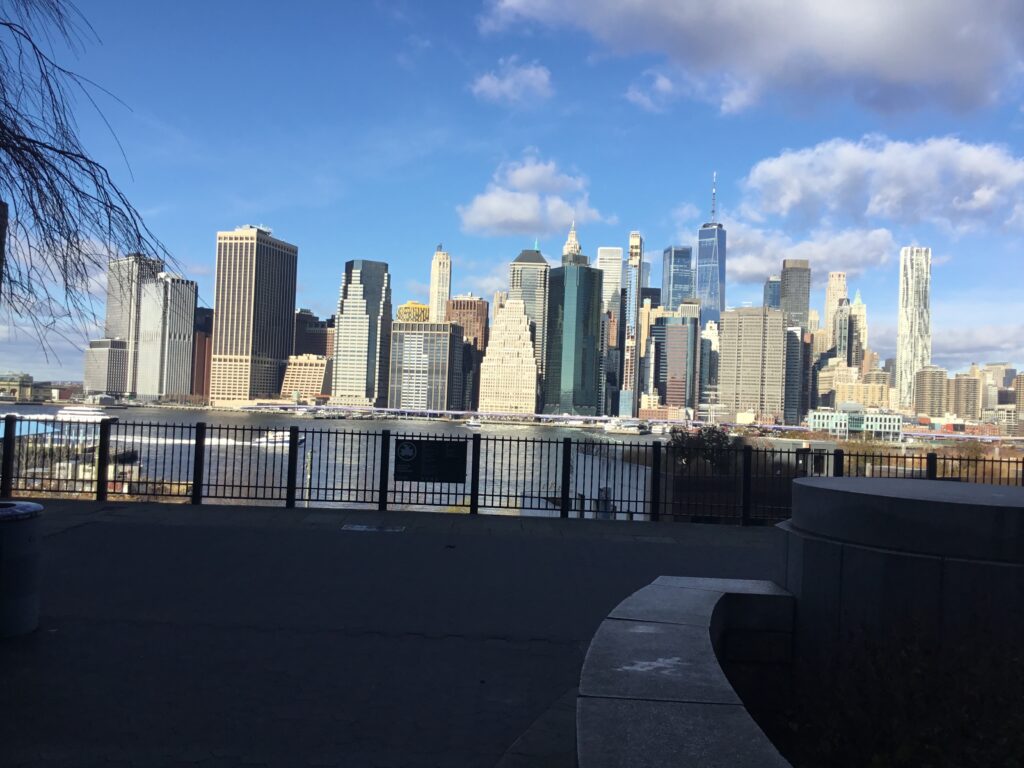 The Lower Manhattan skyline across the East River, seen over the railings of the Brooklyn Heights Promenade on a sunny day