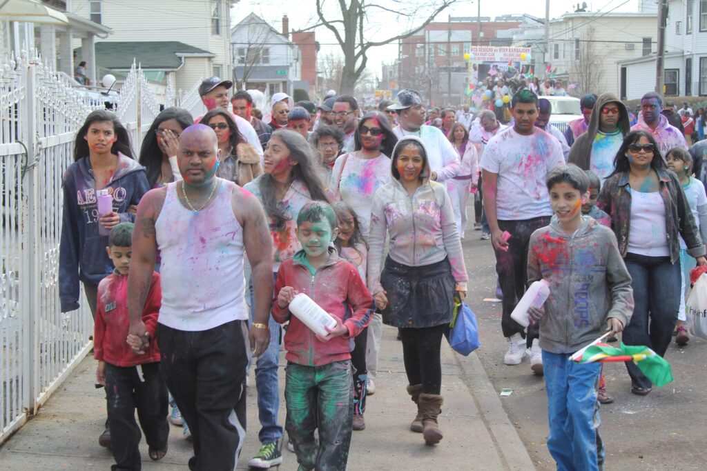 Families covered in colored powder walking in the Phagwah (Holi) parade in Richmond Hill, Queens, with Guyanese flags