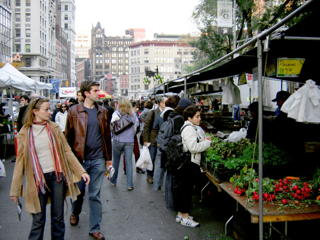 Shoppers walking past farm stalls with radishes and greens at the Union Square Greenmarket