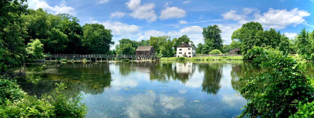 The white stone manor house and wooden gristmill of Philipsburg Manor reflected in the millpond at Sleepy Hollow