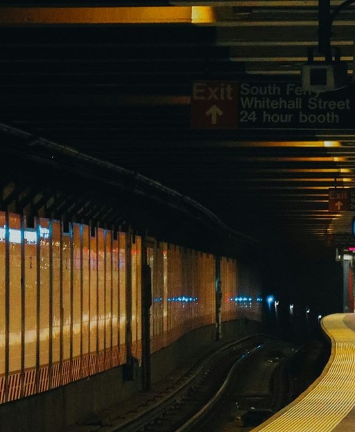 A New York City subway station with a train pulling into the platform, showing passengers on the platform