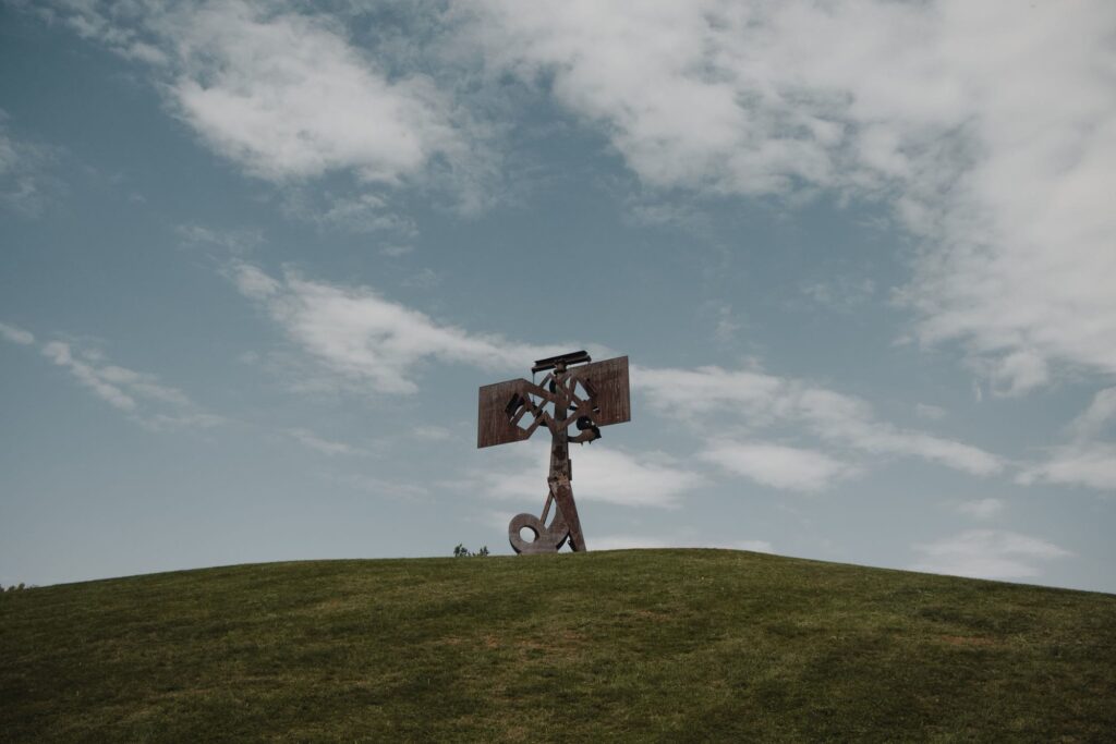 A rust-red steel sculpture standing alone on a grassy hilltop at Storm King Art Center