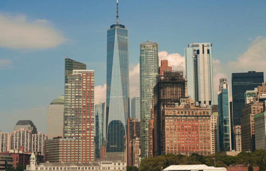 One World Trade Center rising above the towers of Lower Manhattan on a sunny day with a few clouds