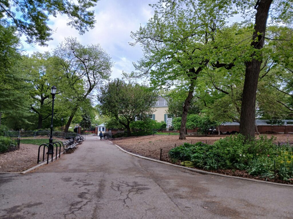 A tree-lined path in Carl Schurz Park with the yellow clapboard Gracie Mansion behind the trees