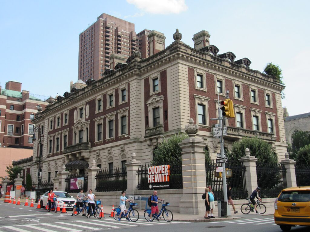 The red-brick and limestone Carnegie Mansion, home of the Cooper Hewitt design museum, with cyclists passing on 91st Street