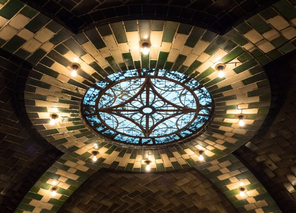 A leaded-glass skylight ringed by green and cream tiles and bare bulbs in the vaulted ceiling of the closed City Hall subway station