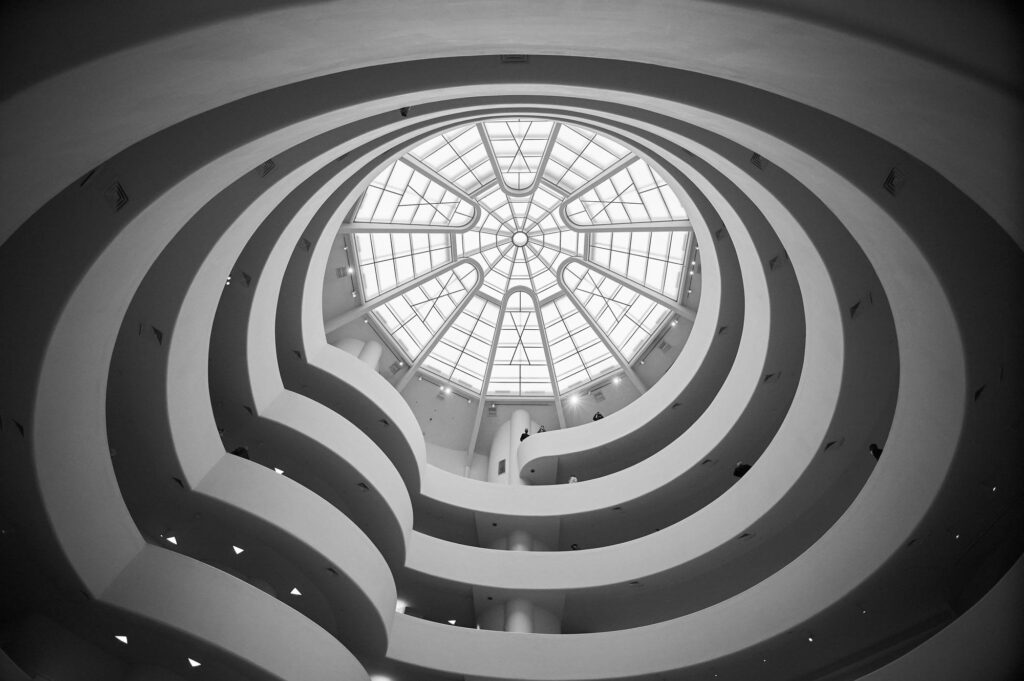 Black-and-white view looking up the white spiral ramps of the Guggenheim rotunda to its glass skylight