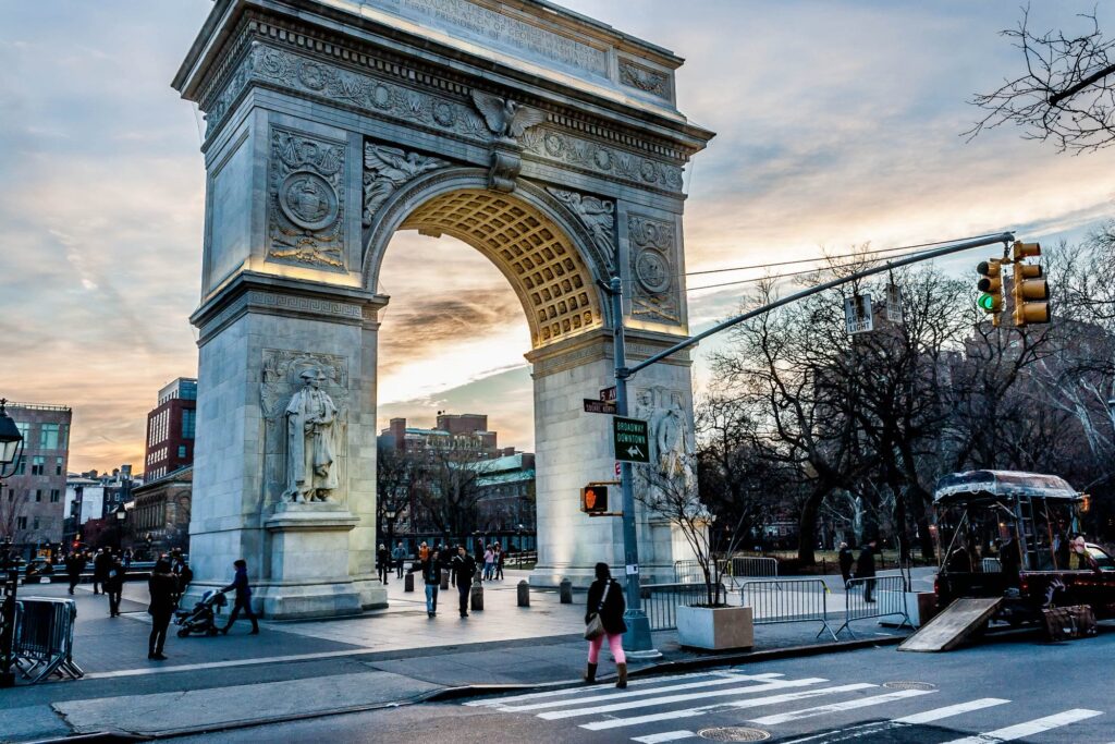 Washington Square Arch in Greenwich Village at sunset, with people crossing Fifth Avenue