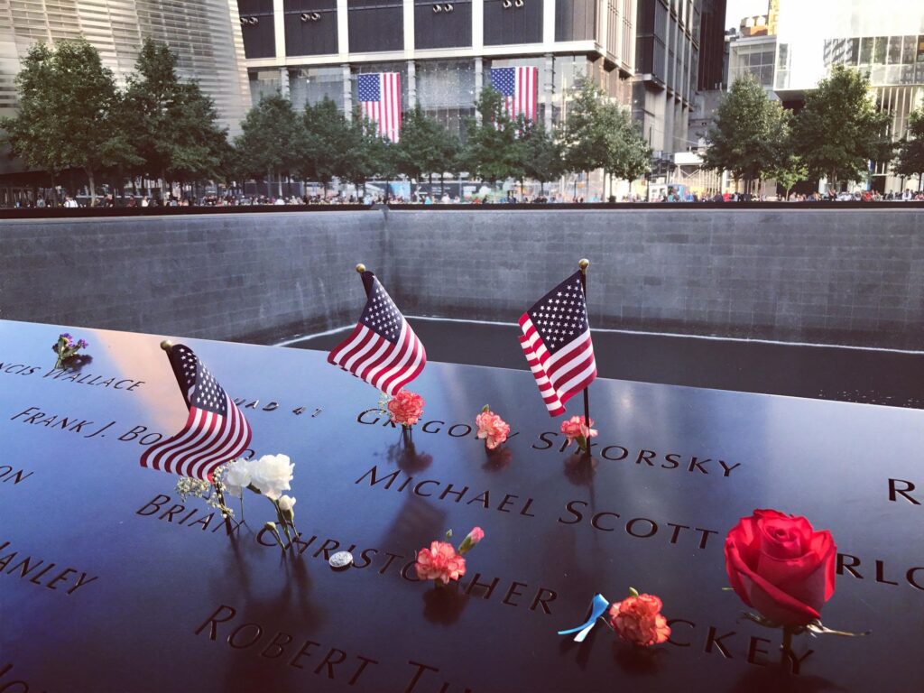 Small American flags and flowers left on the bronze name panels at the 9/11 Memorial pool
