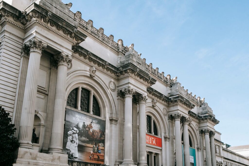 The columns and arched windows of the Metropolitan Museum of Art facade on Fifth Avenue under a blue sky
