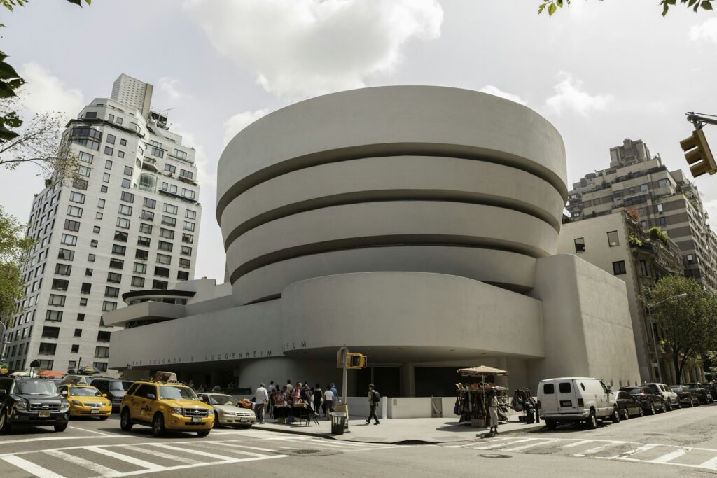 The white spiral exterior of the Guggenheim Museum on a Fifth Avenue corner, with yellow taxis and visitors outside