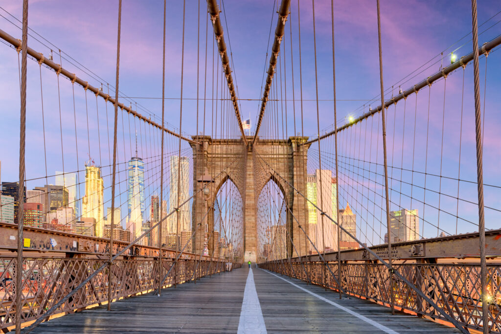 The timber promenade of the Brooklyn Bridge at dawn, with the stone tower and Lower Manhattan skyline ahead