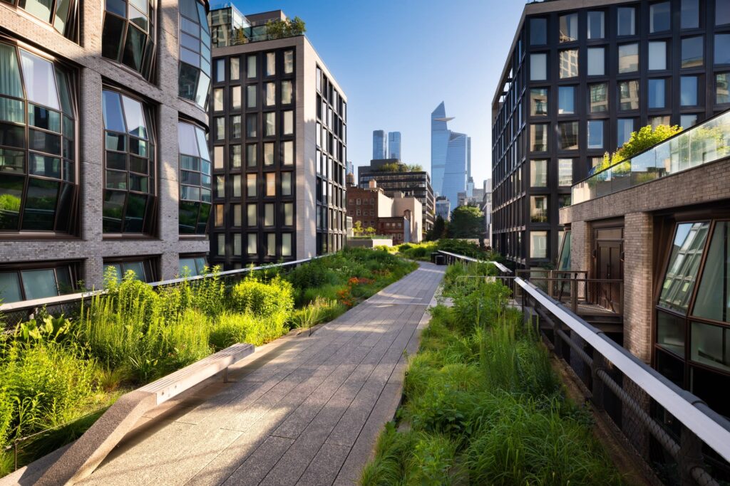The planted walkway of the High Line between Chelsea apartment buildings, with the Hudson Yards towers ahead
