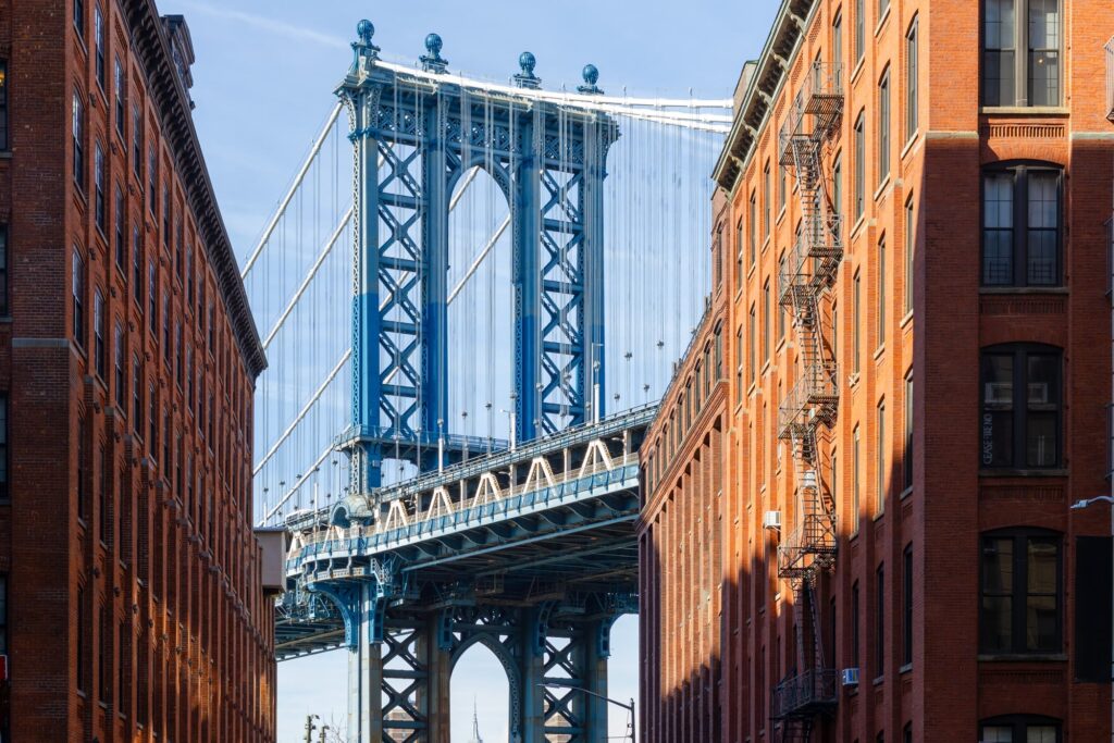 A tower of the Manhattan Bridge framed between red-brick warehouse buildings in DUMBO