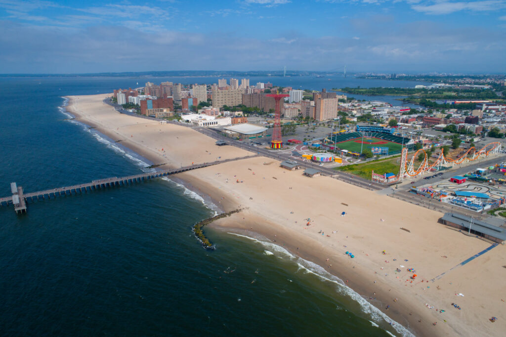 Coney Island from the air: the beach, the fishing pier, the red Parachute Jump tower and an orange roller coaster