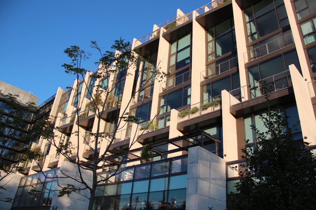 The pale stone and glass facade of 1 Hotel Brooklyn Bridge, its balconies lined with planters, in evening sun