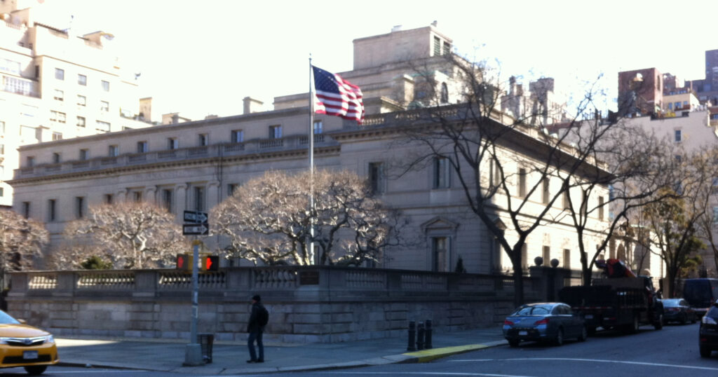 The Frick Collection's limestone mansion behind its low balustrade wall at Fifth Avenue and 70th Street, with an American flag flying