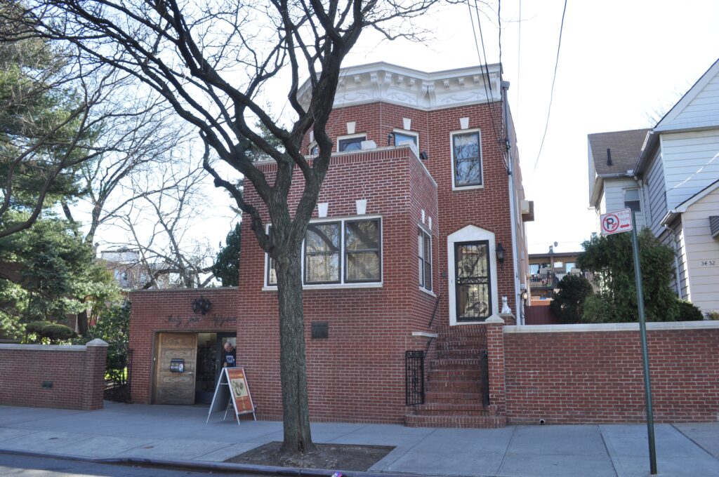 The red-brick Louis Armstrong House on a residential street in Corona, Queens, with a museum sign by the door