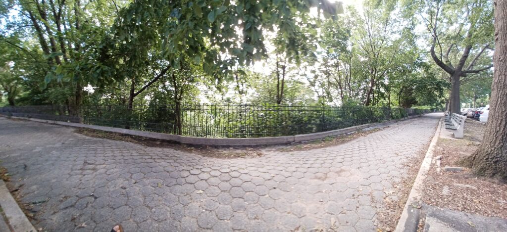 Wide-angle view of the hexagon-paved path in Shore Road Park, Bay Ridge, with an iron railing, trees and park benches