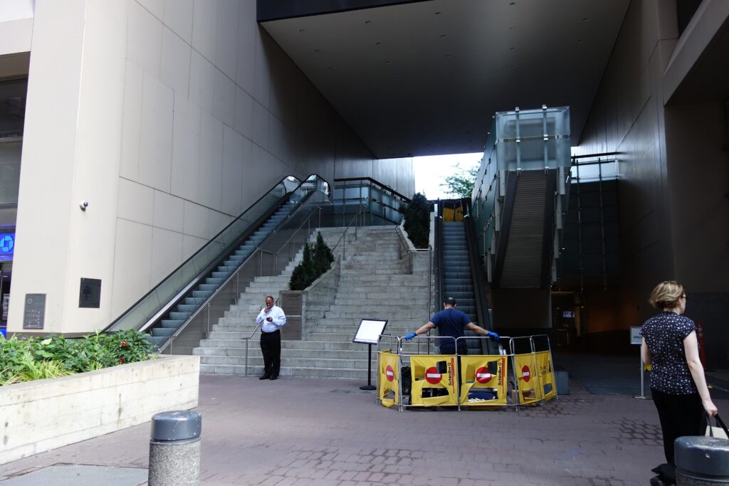 Wide concrete stairs and escalators rising from the street to the Elevated Acre at 55 Water Street, with its name plaque at the foot