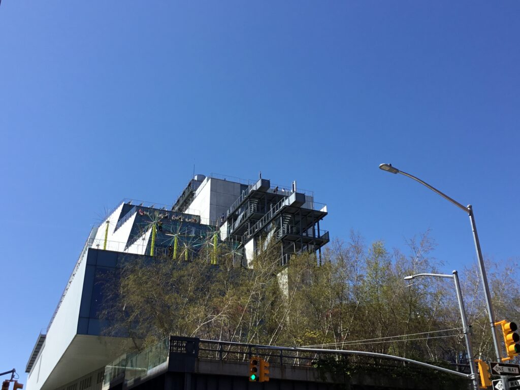 The stepped terraces and outdoor stairs of the Whitney Museum rising above the trees of the High Line