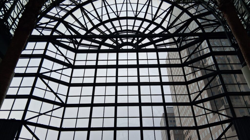 The arched glass and steel wall of the Winter Garden atrium at Brookfield Place, with palm trunks at the edges and an office tower beyond