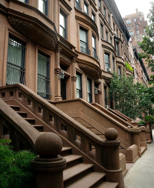 A tree-lined street of brownstone row houses with ornate stoops in New York City