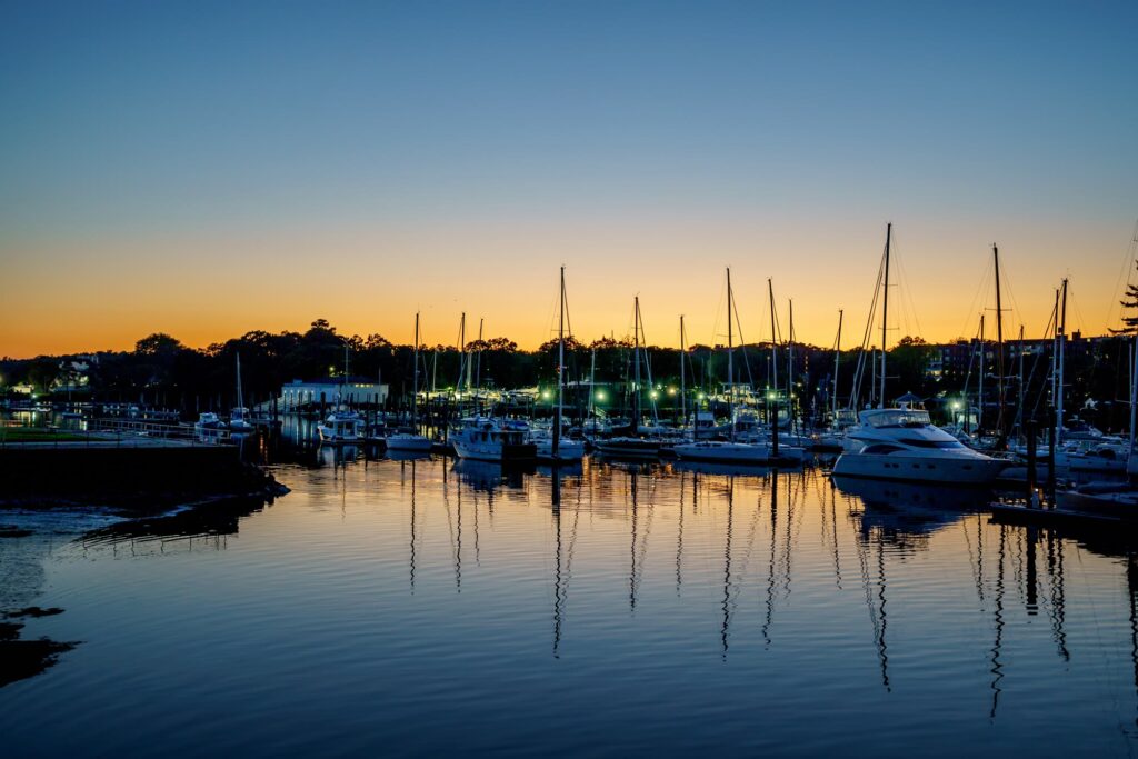 Sailboats and motor yachts moored in a calm marina on City Island at dusk, their masts reflected in the water