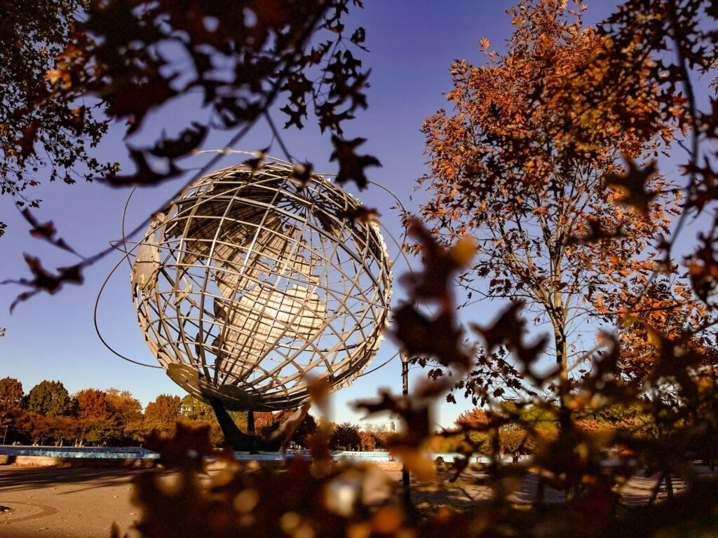 The steel Unisphere globe in Flushing Meadows-Corona Park, framed by orange fall leaves against a blue sky