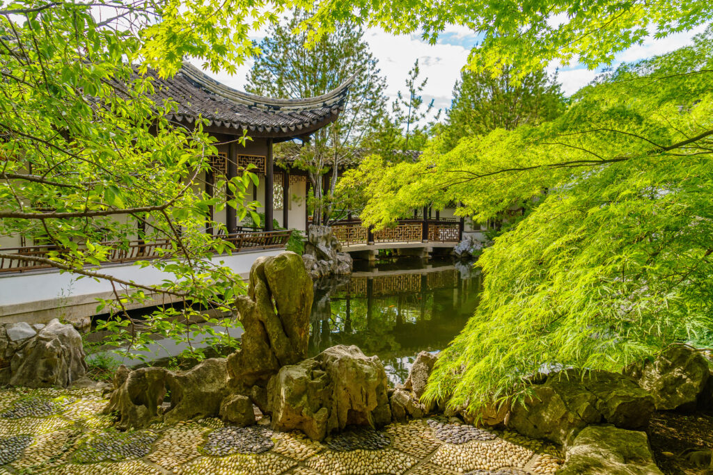 A curved-roof pavilion and covered walkway beside a pond and stone rockery in the New York Chinese Scholar's Garden at Snug Harbor