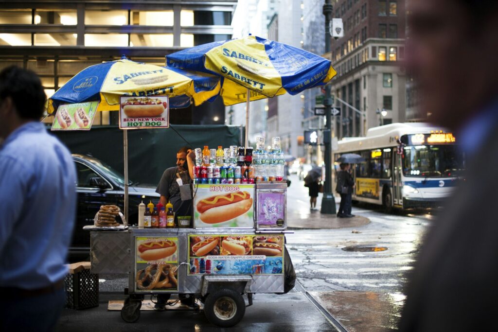 A hot dog vendor cart on a busy New York City street intersection