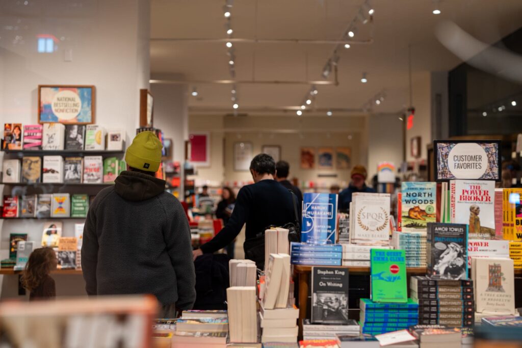 Shoppers in winter hats browsing tables and shelves of new books in a brightly lit New York bookstore