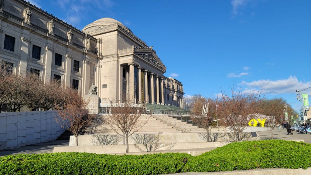 The columned Beaux-Arts facade and wide front steps of the Brooklyn Museum under a blue spring sky