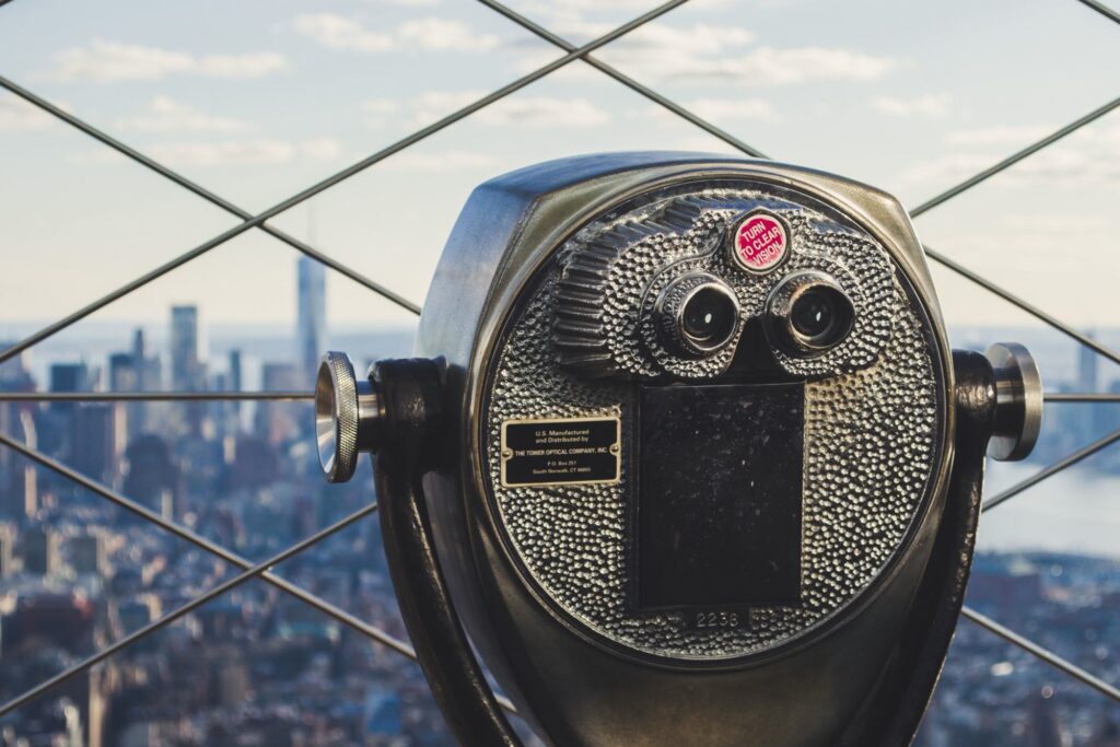 Coin-operated binoculars behind the diamond-pattern safety fence of the Empire State Building's 86th-floor deck, Lower Manhattan beyond