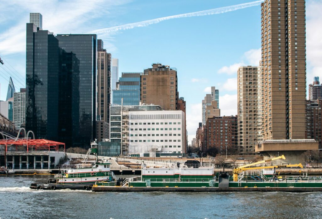 Green and white industrial barge on the East River passing Manhattan