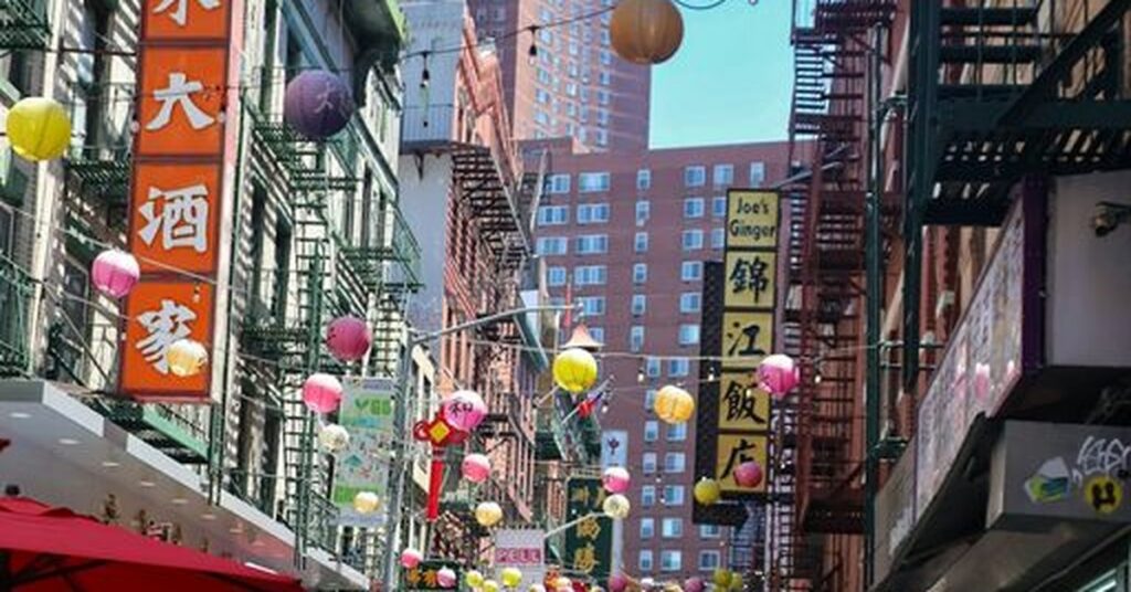 Crowded Mott Street in New York Chinatown beneath hanging lanterns